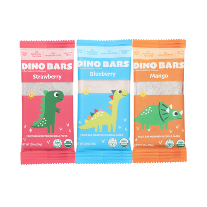 Three Dino Bars fruit bars in individual colorful wrappers, shown side by side on a plain white background. The wrappers are pink for Strawberry, light blue for Blueberry, and orange for Mango, each featuring a cartoon dinosaur illustration and the brand name DINO BARS.